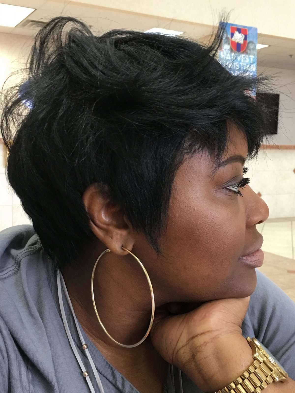 Woman with voluminous black pixie hair wearing gold hoop earrings and a gold watch.