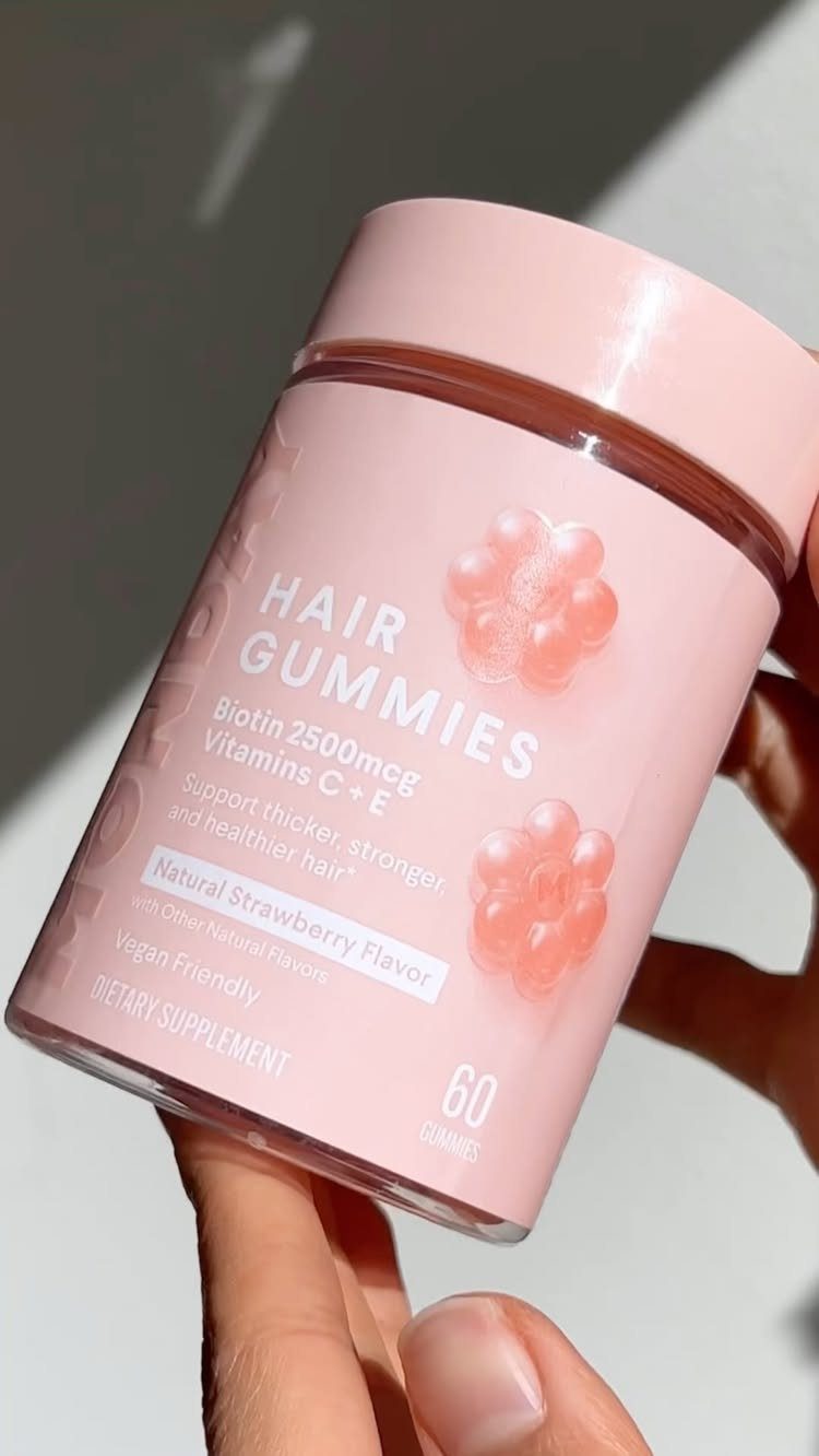 Pink bottle of biotin hair gummies held by a hand against a light background.