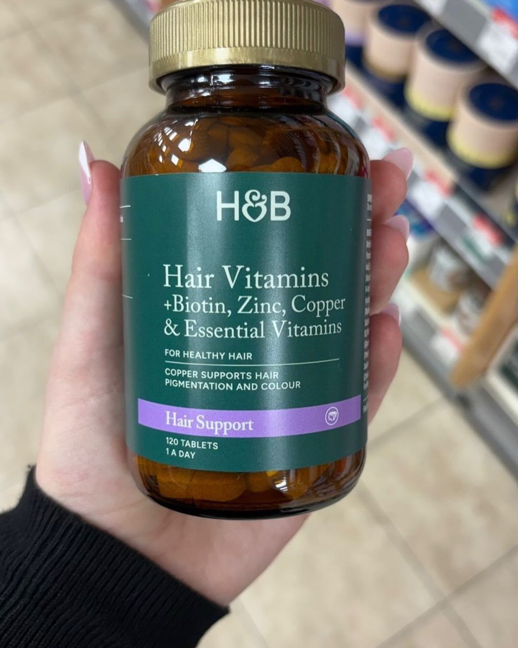 Brown glass bottle of hair vitamins containing biotin held by a person's hand.