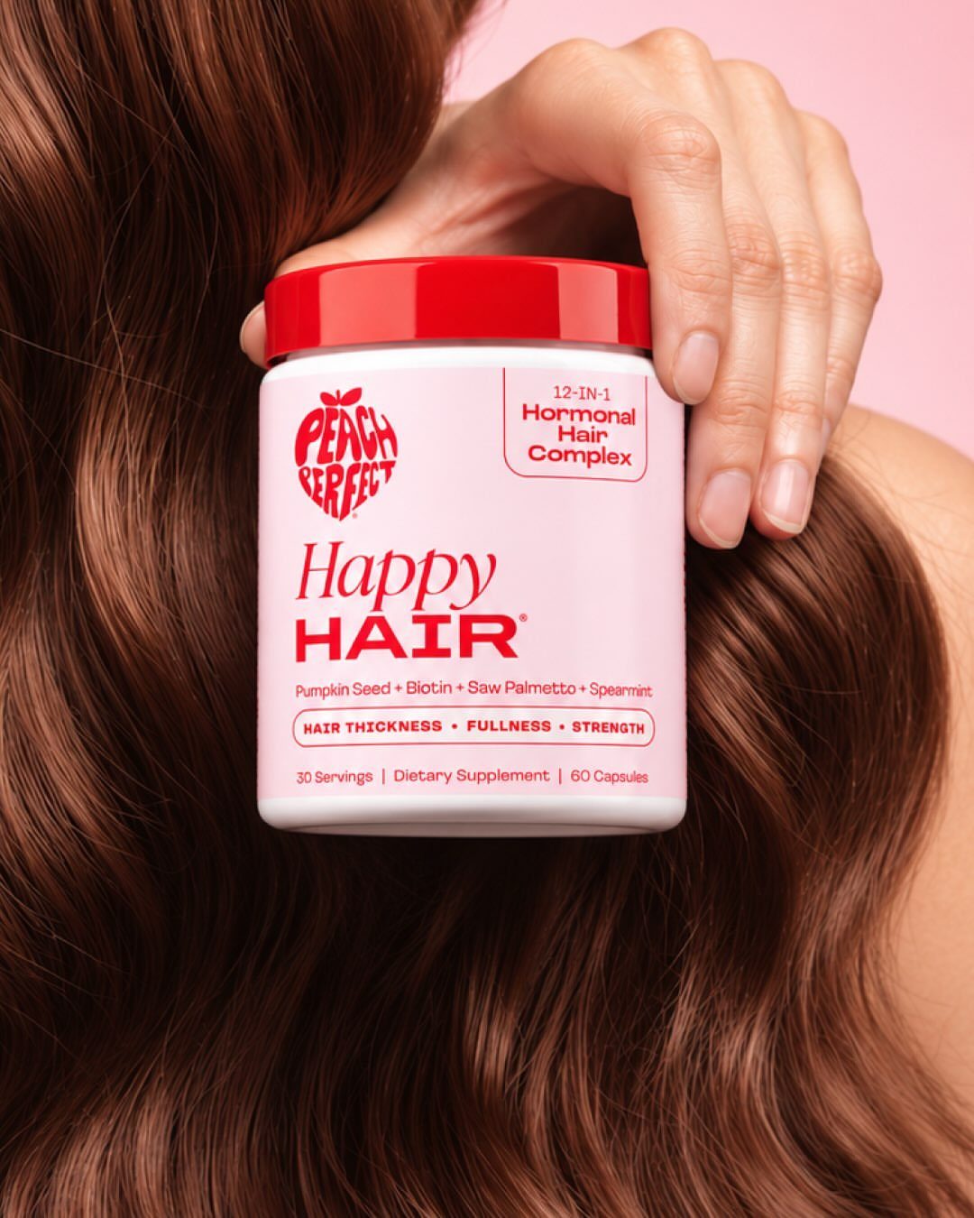 White supplement bottle for hair growth held against long wavy brown hair.