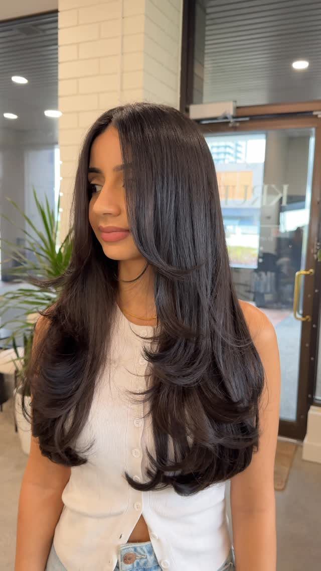 Woman with long dark hair styled in voluminous face-framing waves and layers.