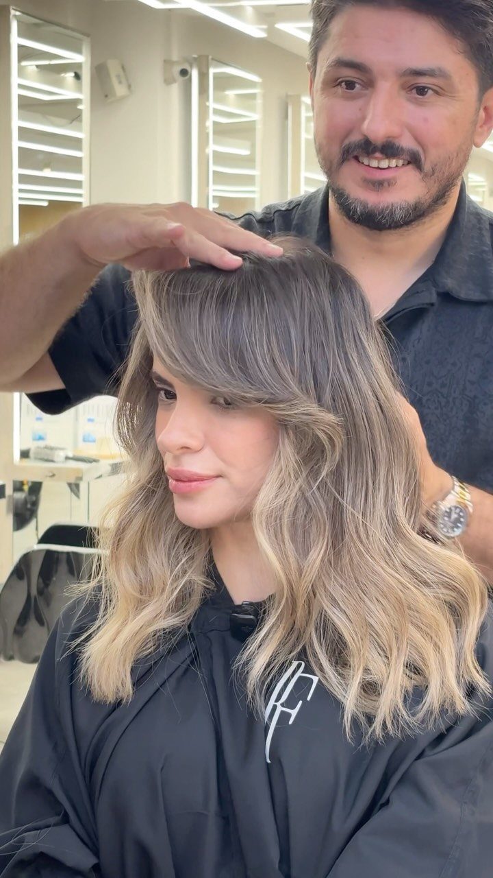 Woman with soft face-framing waves and blonde highlights in a hair salon.