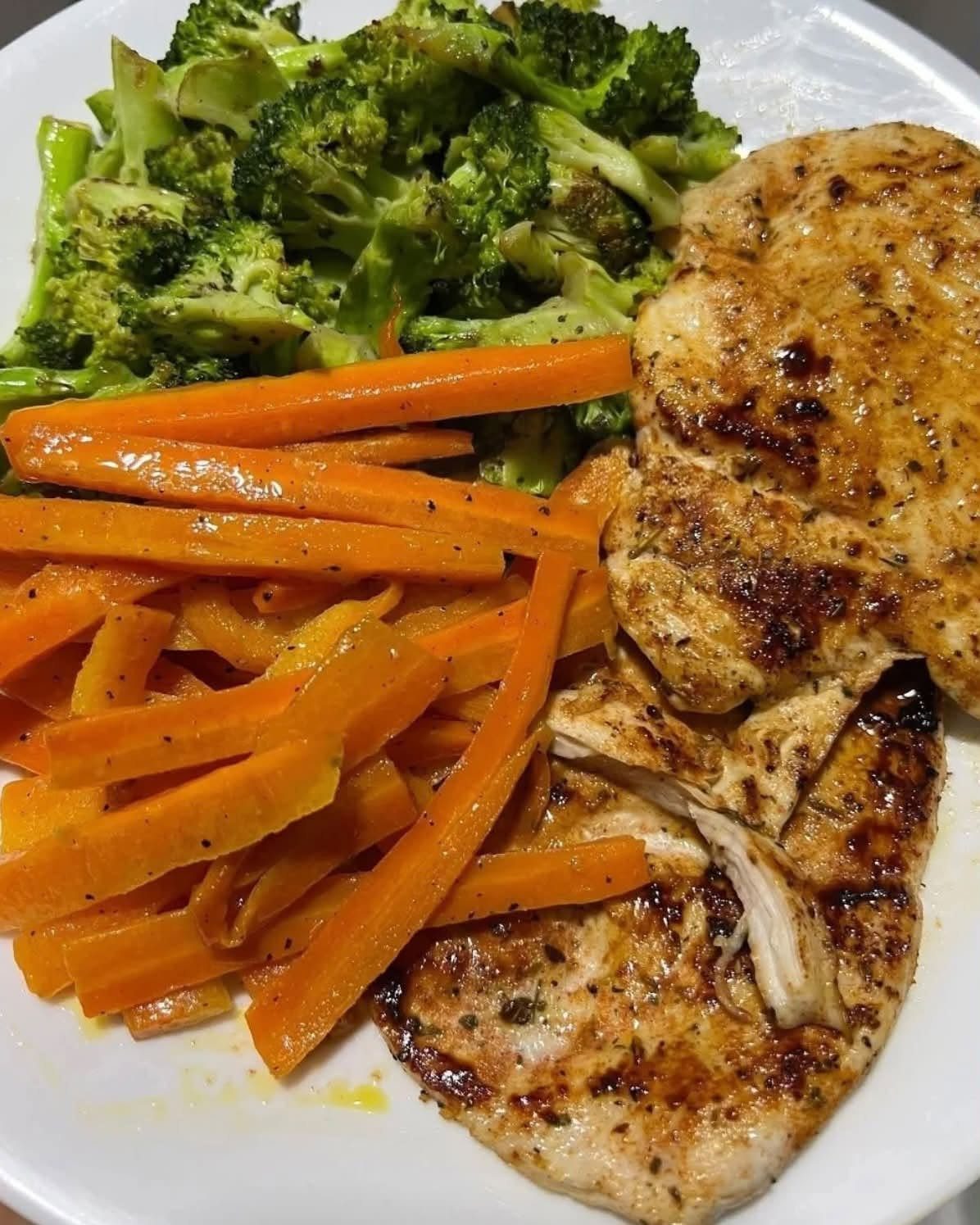 Grilled chicken breasts served with steamed broccoli and sliced carrots on a white plate.