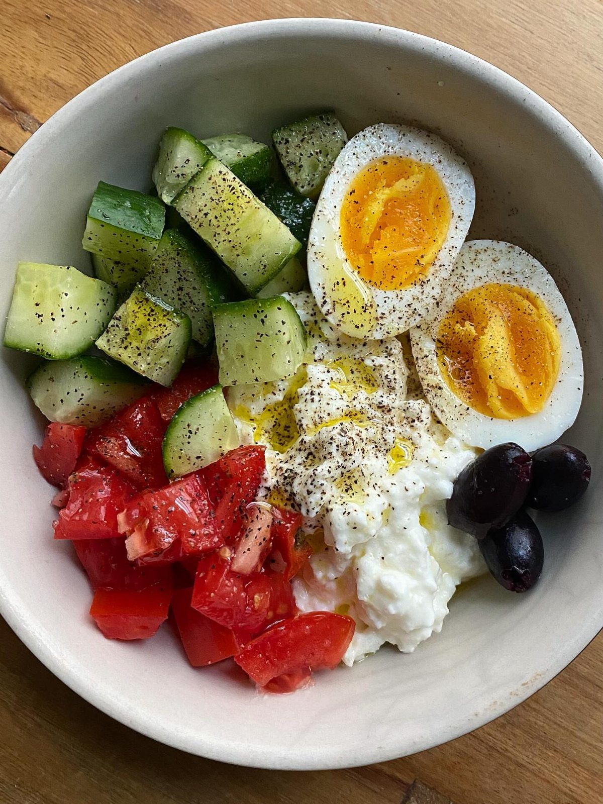 Cottage cheese bowl with hard boiled eggs, cucumbers, tomatoes, and black olives.