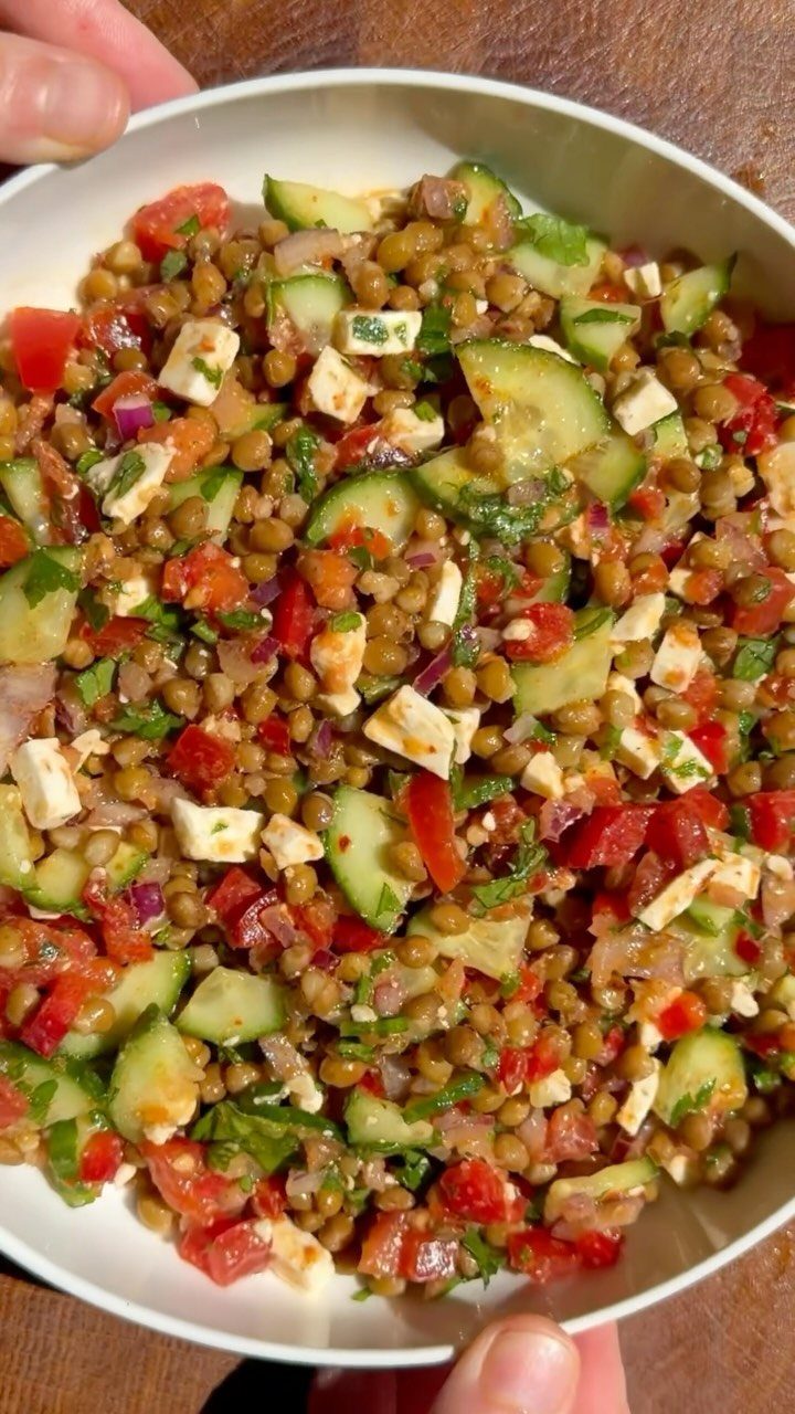 Lentil salad with cucumbers, tomatoes, and feta cheese in a white bowl.