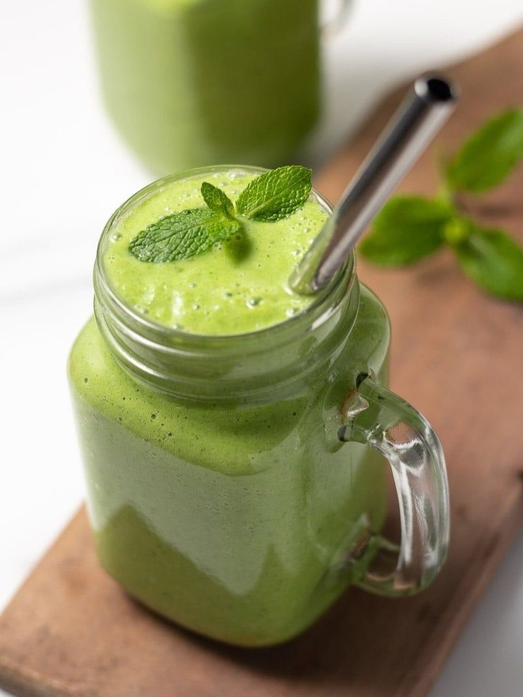 Green spinach smoothie in a mason jar with a metal straw and mint leaves