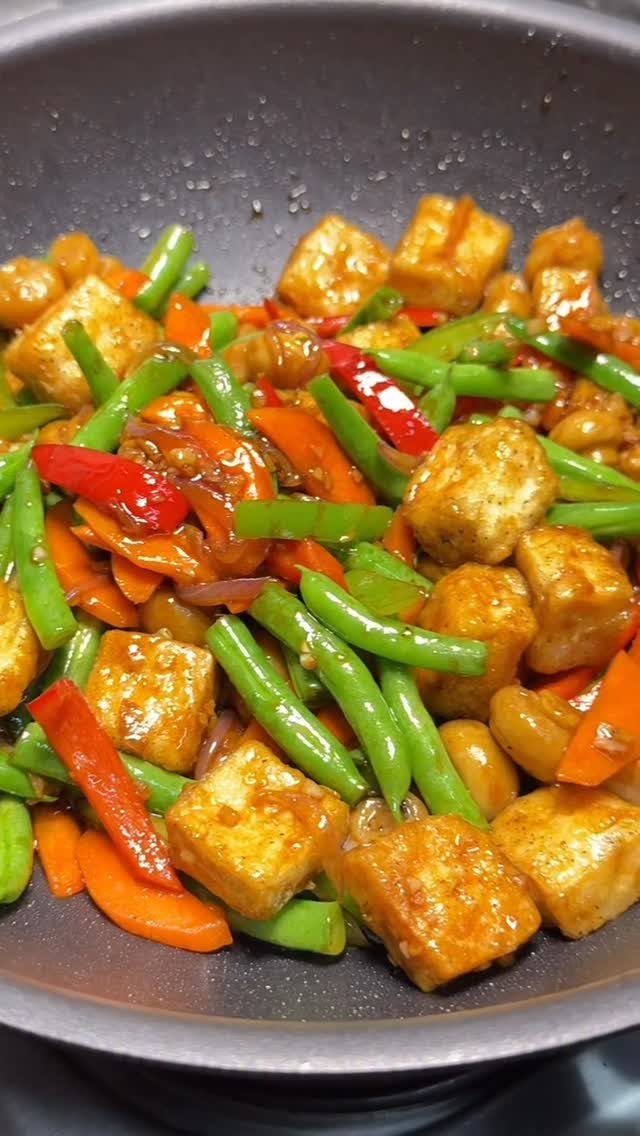 Stir-fry with tofu, green beans, carrots, and red peppers in a cooking pan.