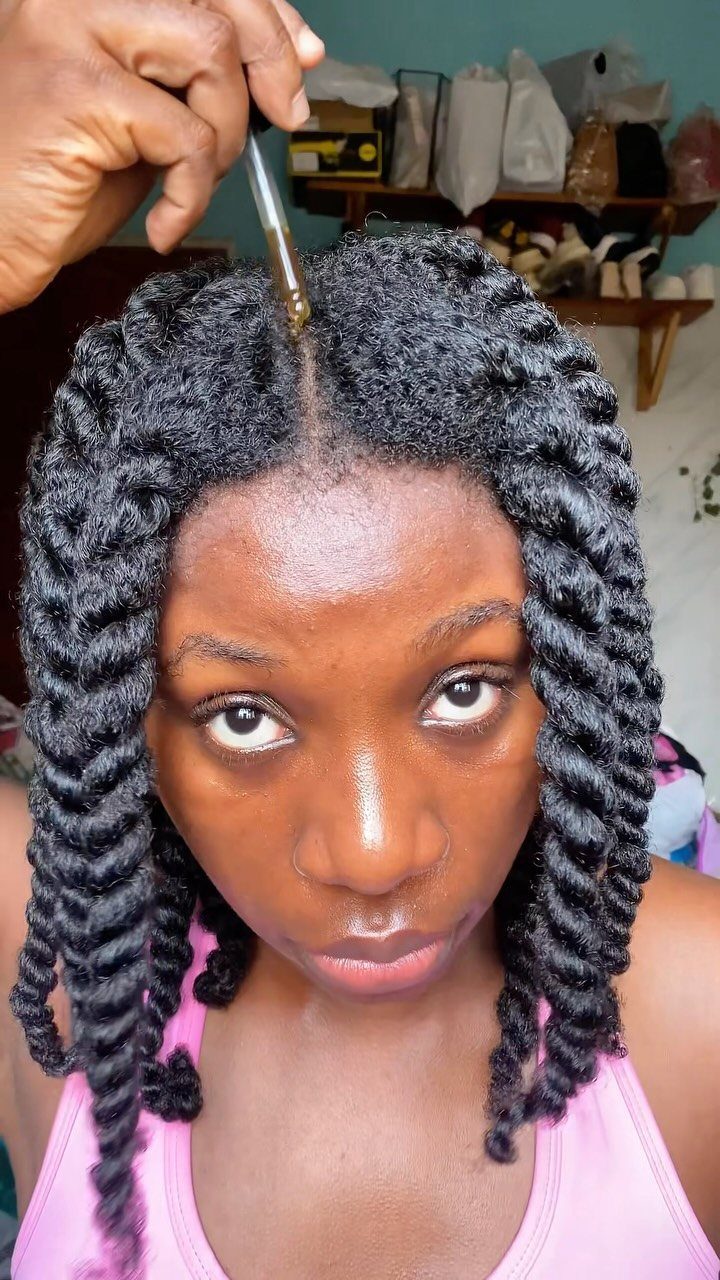 Woman with twisted black hair receiving a scalp treatment from a glass dropper.