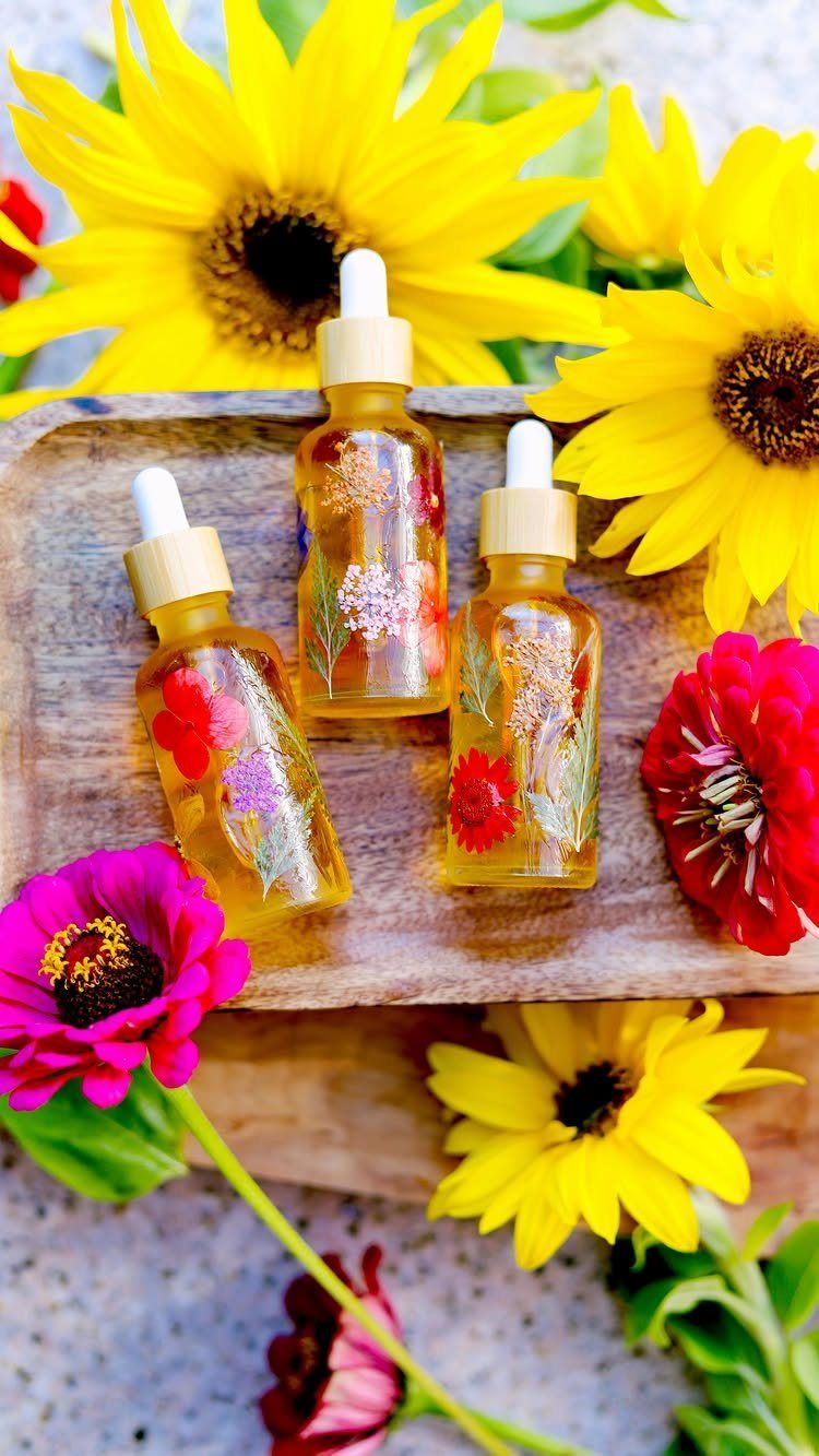 Three glass dropper bottles with botanical oils on a wooden tray among sunflowers.