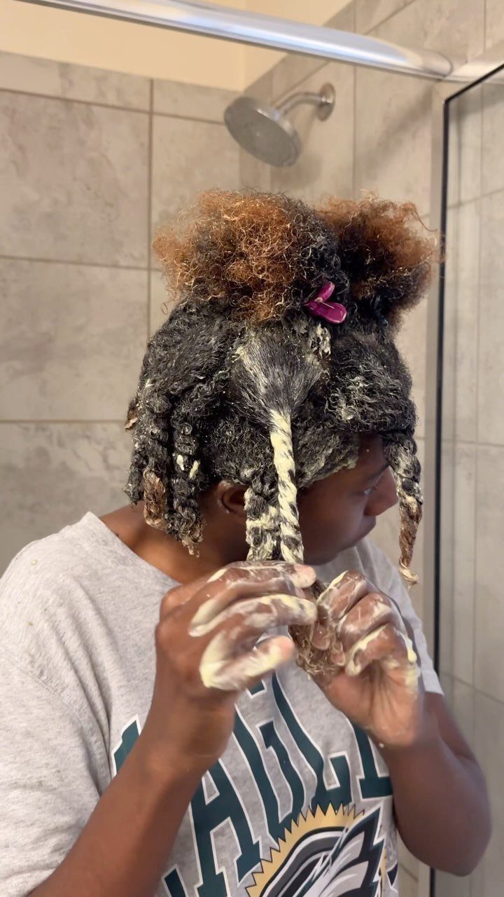 Person applying a creamy homemade hair mask to their curly hair in a shower.