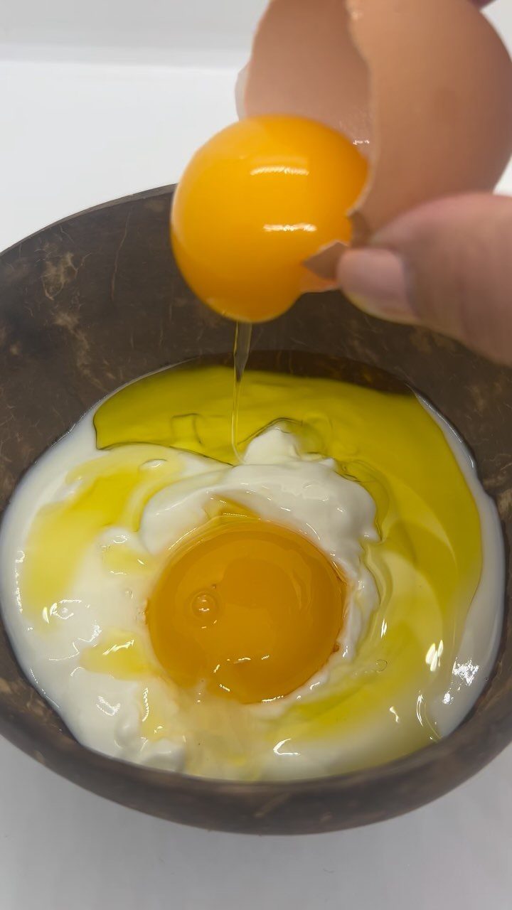 Raw egg being cracked into a bowl of yogurt and oil for hair mask.