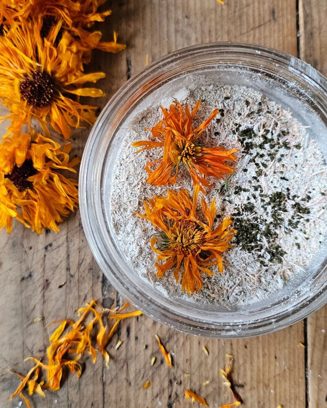 Homemade scalp scrub in a glass jar decorated with orange flowers on wood.