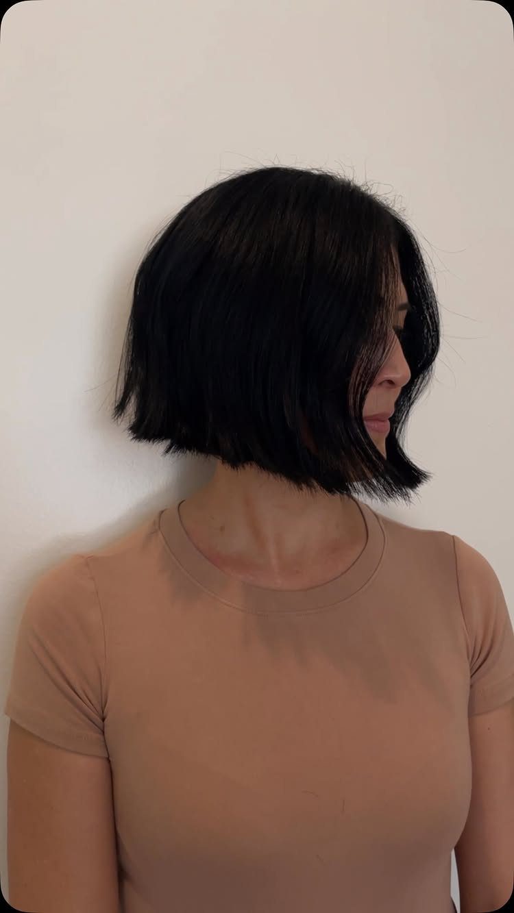 Woman with a chin-length straight black blunt bob haircut against a white wall.