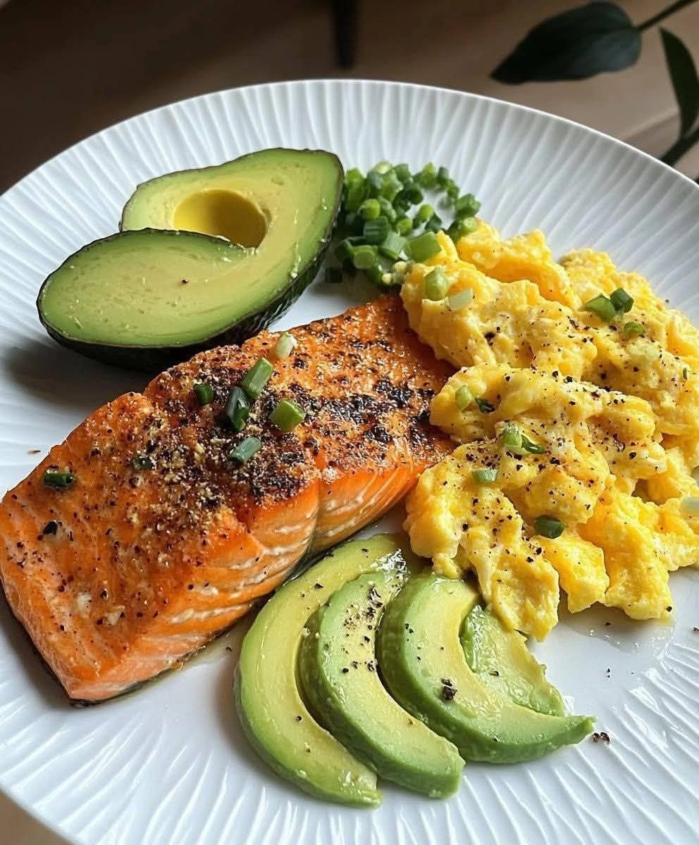 Cooked salmon fillet, scrambled eggs, and sliced avocado on a white plate.