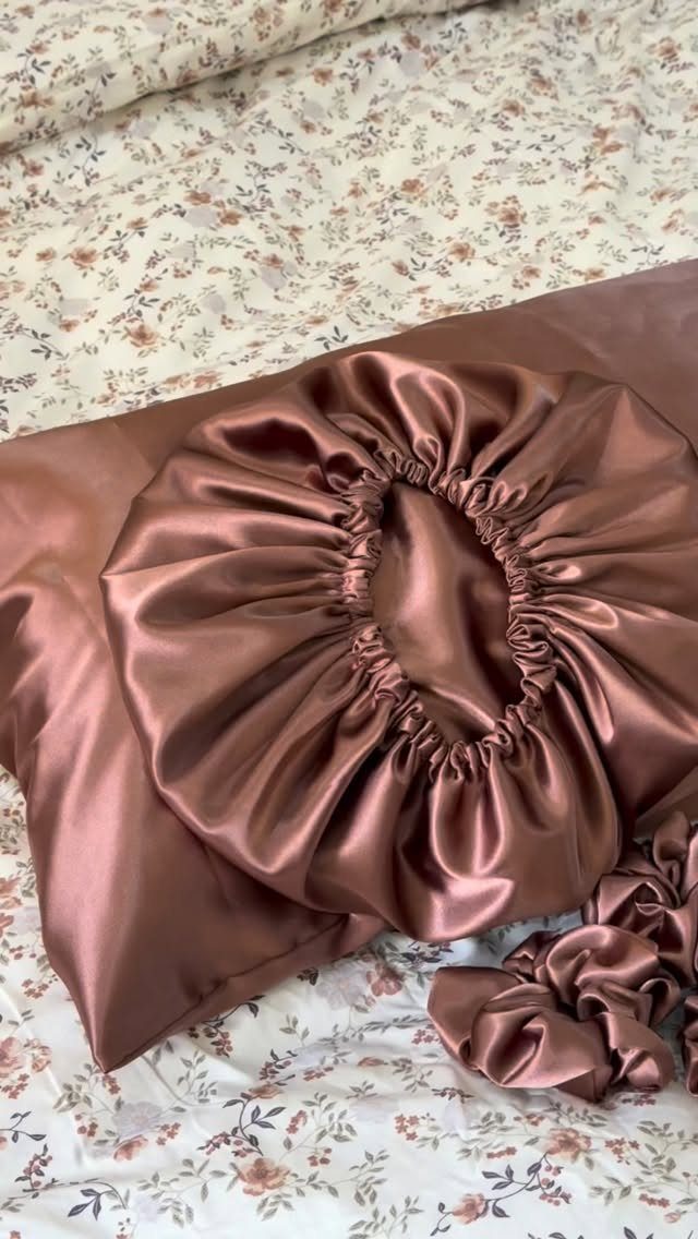 Brown satin pillowcase with a matching satin bonnet and scrunchie on floral bedding.