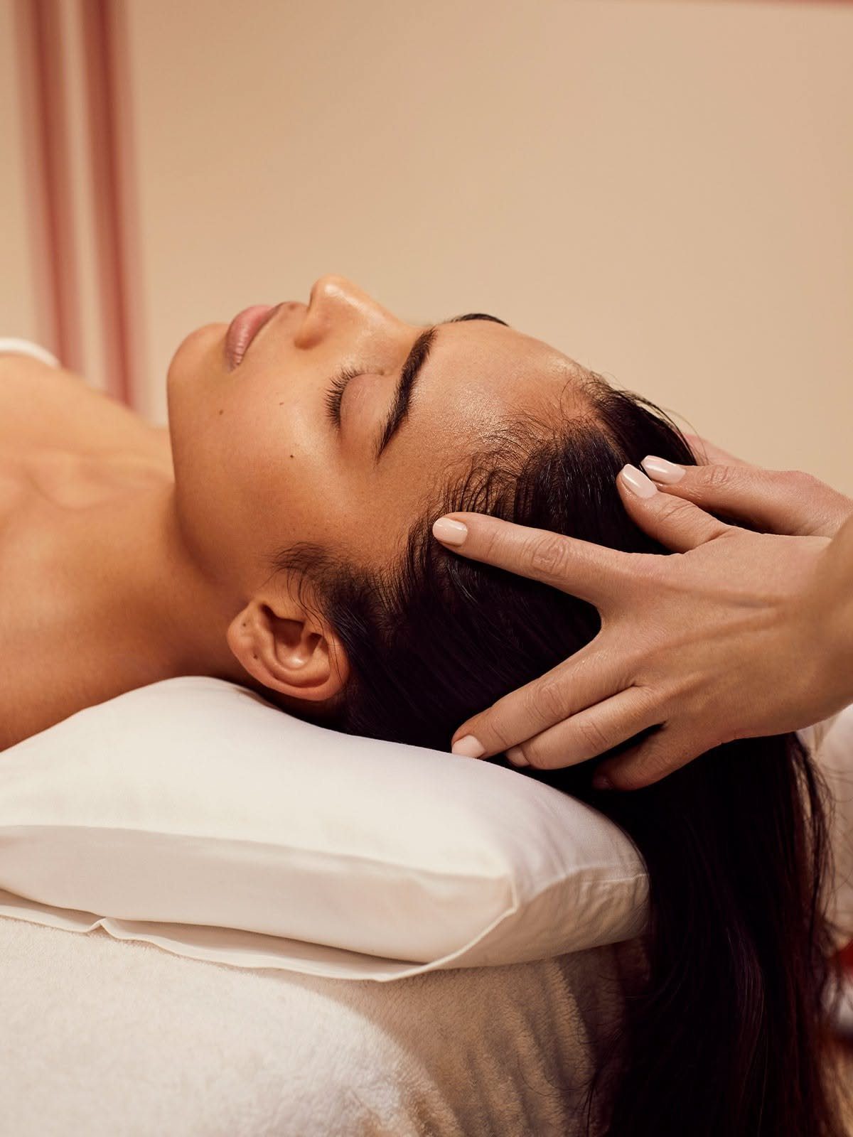 Woman receiving a scalp massage with fingertips while lying on a white pillow