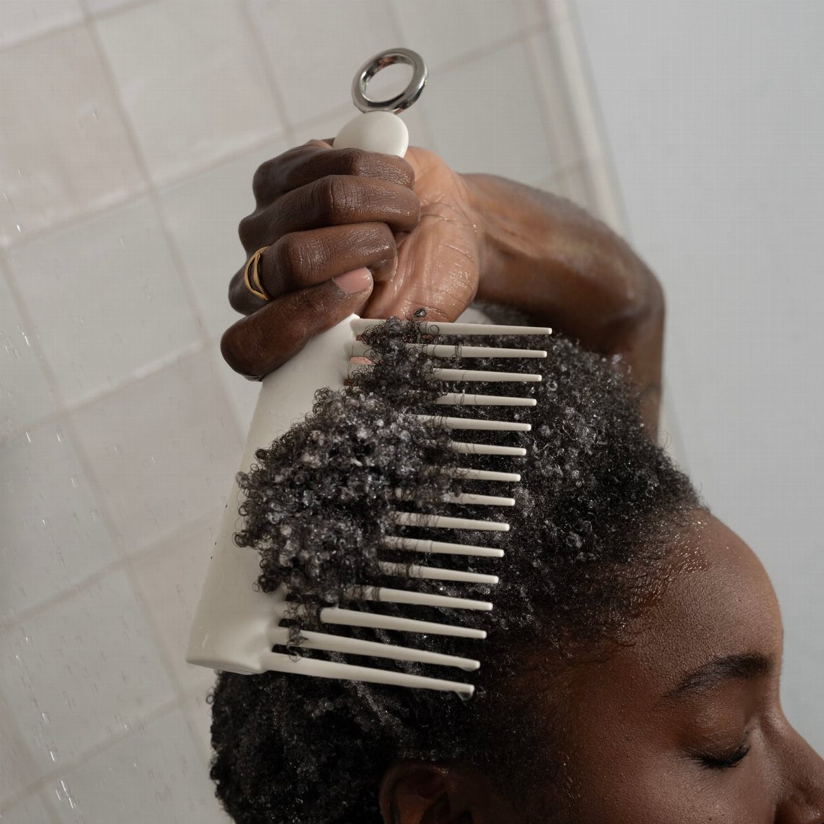Person with curly hair using a wide-tooth comb to detangle hair in a shower.