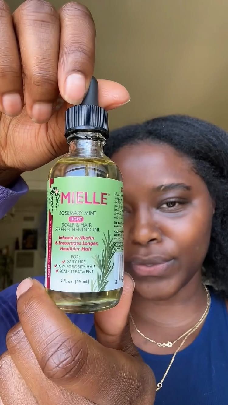 Mielle Rosemary Mint hair oil bottle held up by a person.