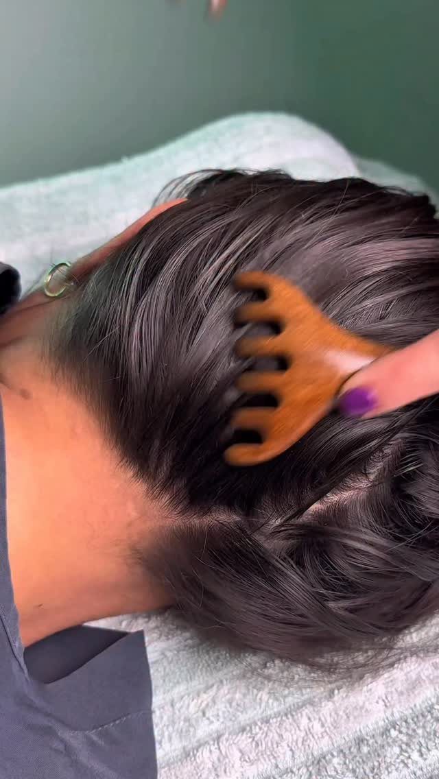 Wooden comb massaging the scalp of a person with dark hair on a towel