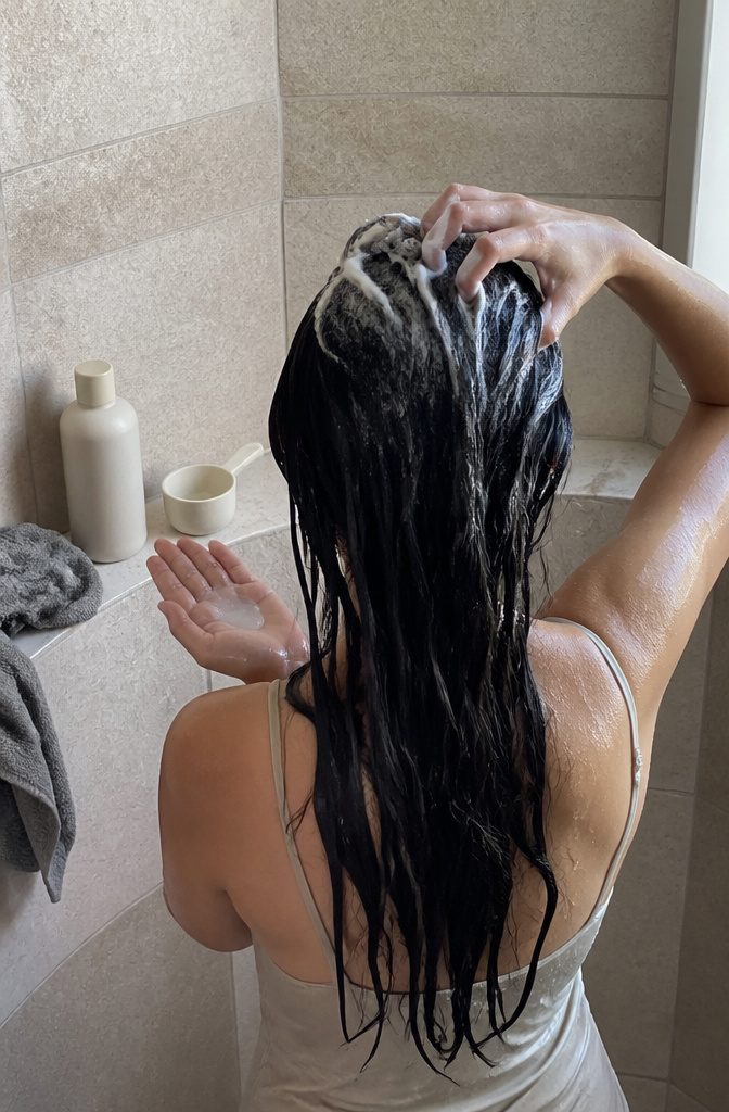 Wet hair roots covered in white shampoo lather with shampoo in a palm