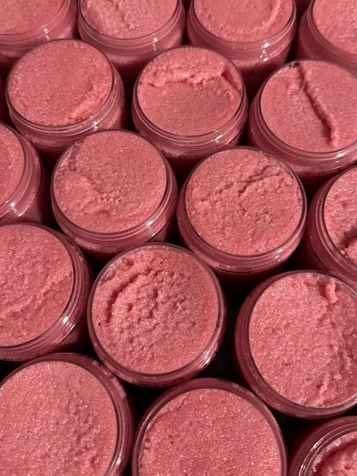 Pink grainy scrub in multiple clear plastic jars arranged in a close-up grid.