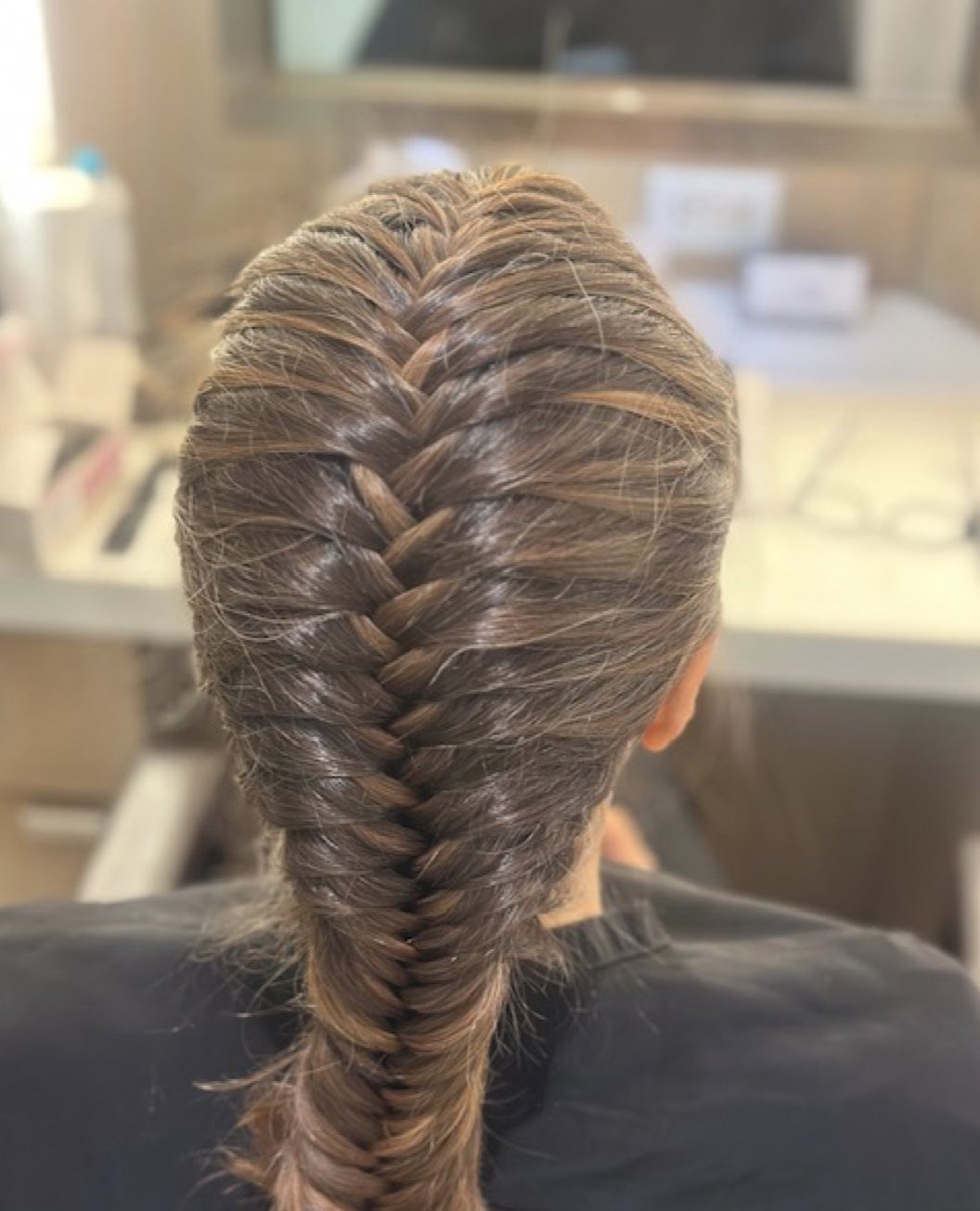 Brown hair styled in a thick, textured fishtail braid from crown to nape.
