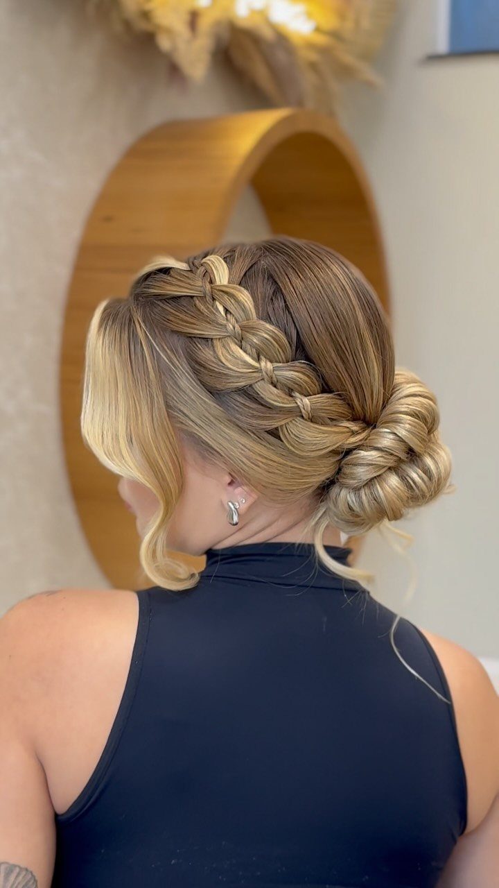 Blonde woman with a side French braid ending in a low bun.