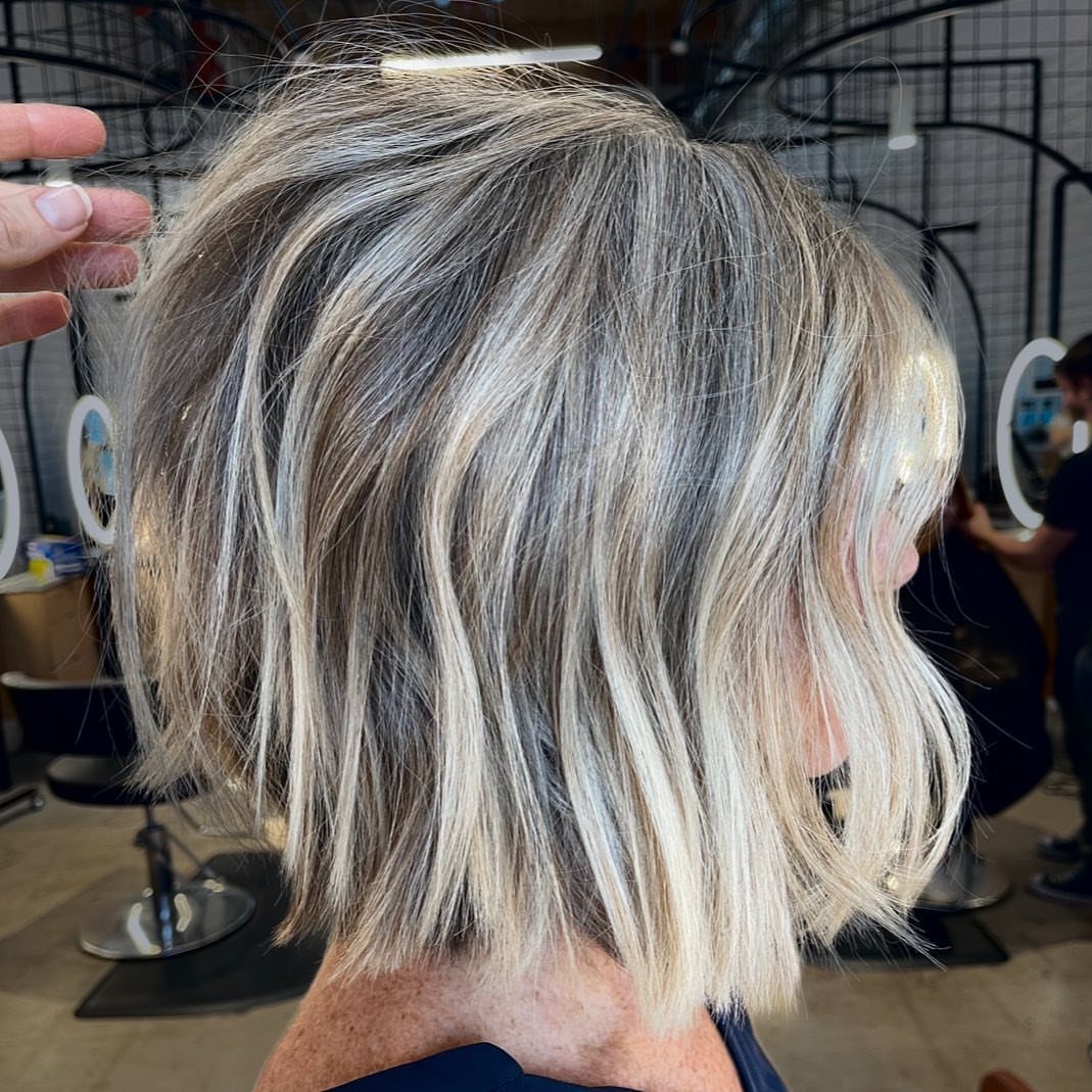 Short layered bob haircut with blonde and grey highlights on a mature person.