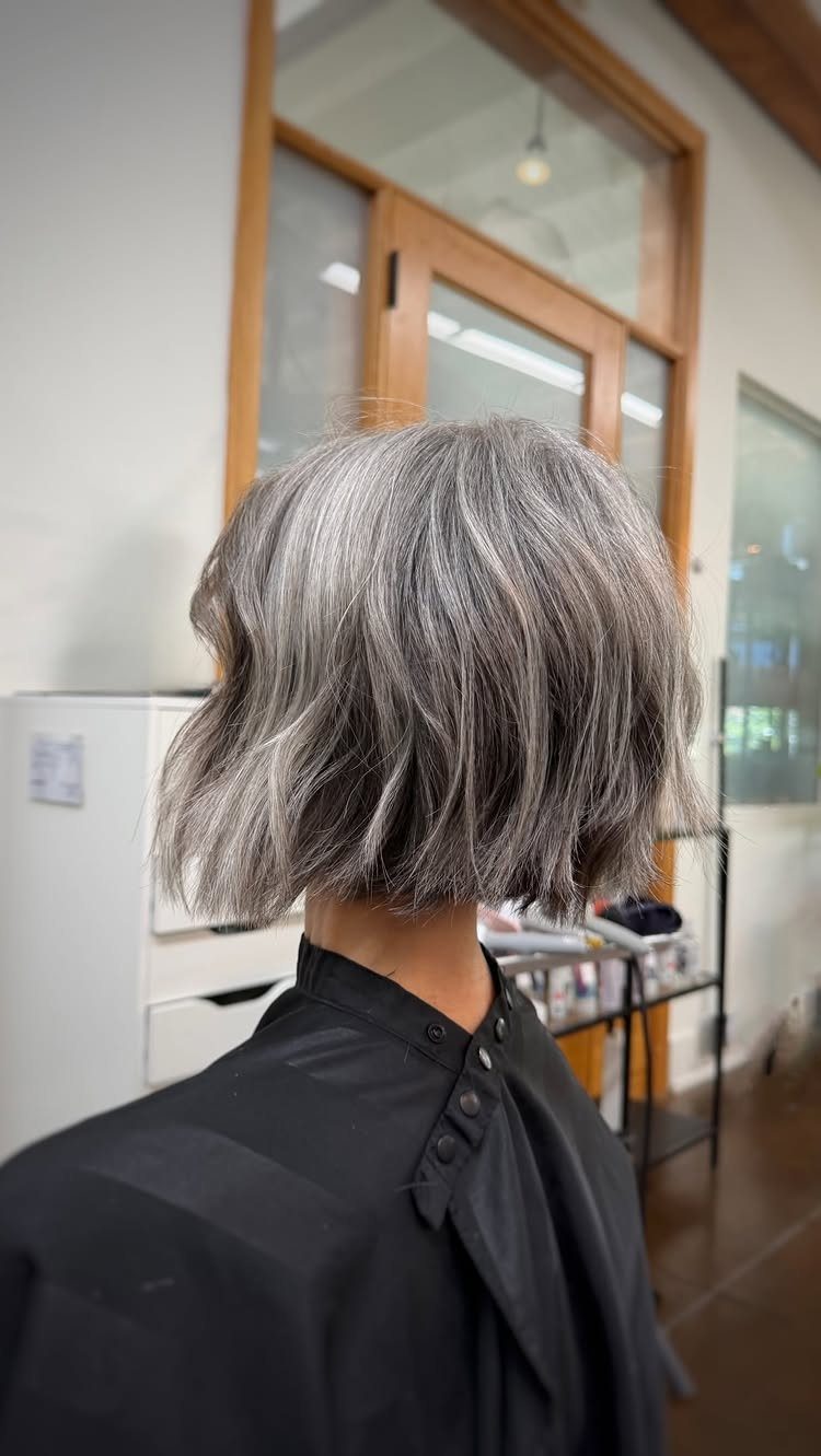Textured gray bob hairstyle on a person wearing a black salon cape.