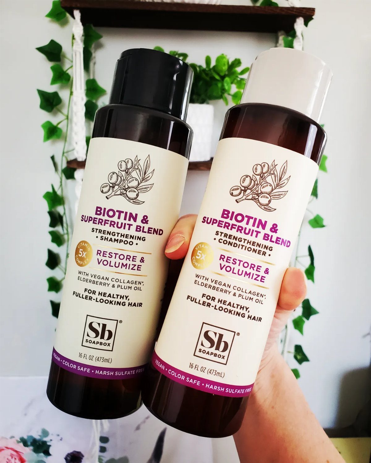 Two Soapbox Biotin and Superfruit Blend shampoo and conditioner bottles held by a hand.