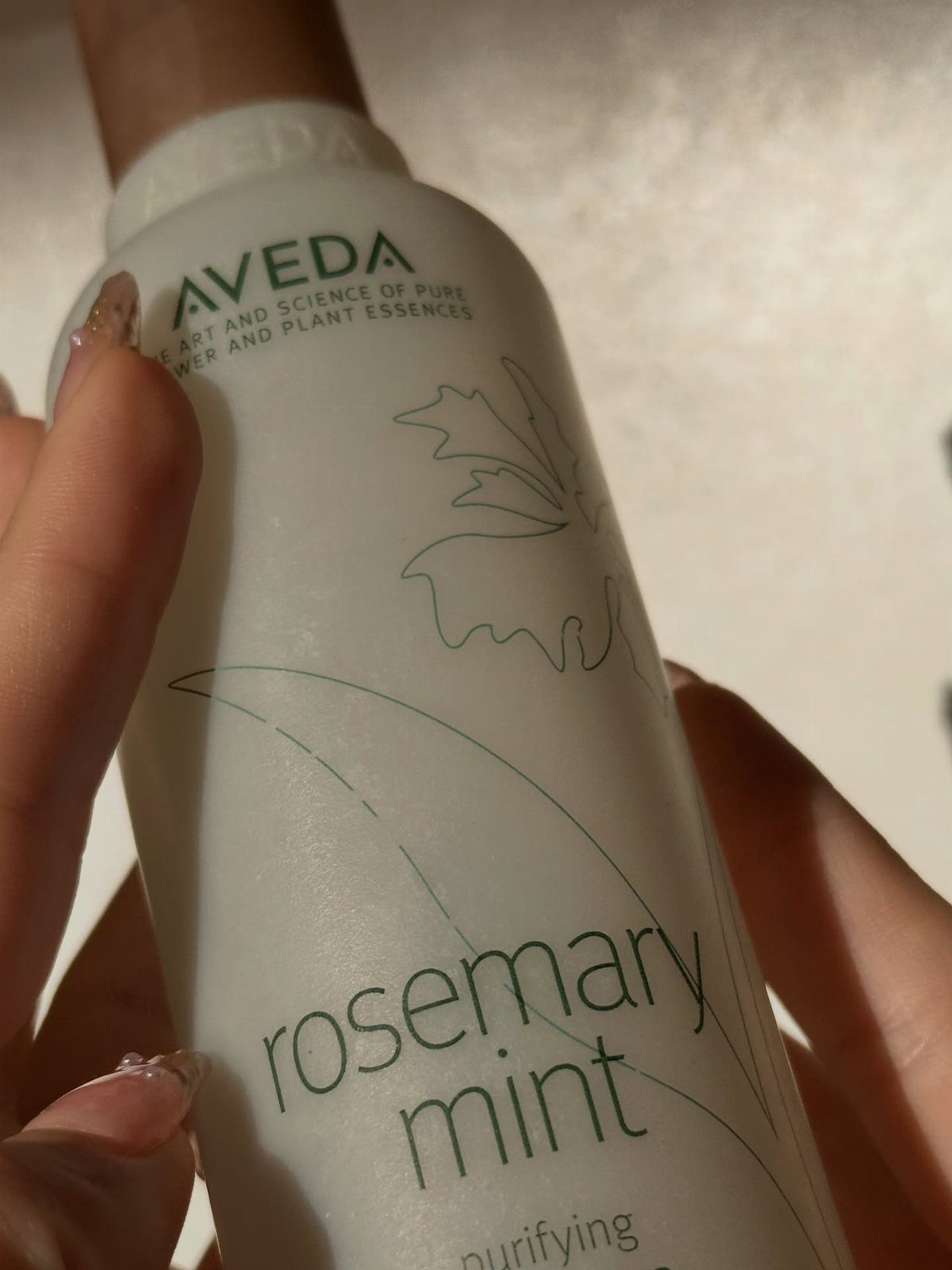 Aveda rosemary mint purifying shampoo bottle held by two hands.