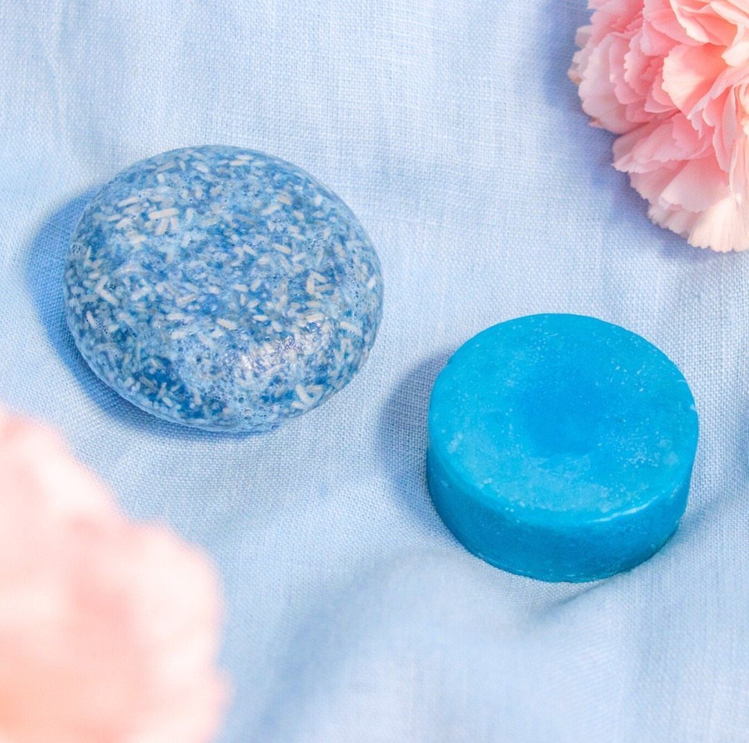 Two round blue shampoo bars on light blue fabric with pink flowers.