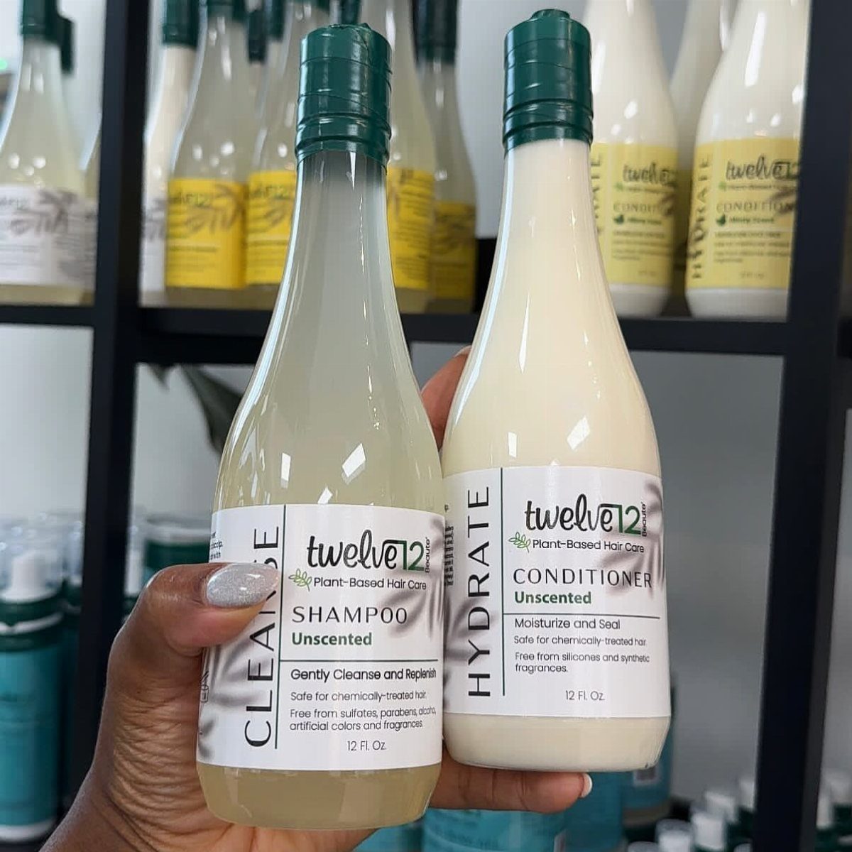 Two bottles of Twelve Twelve unscented shampoo and conditioner held in a hand.