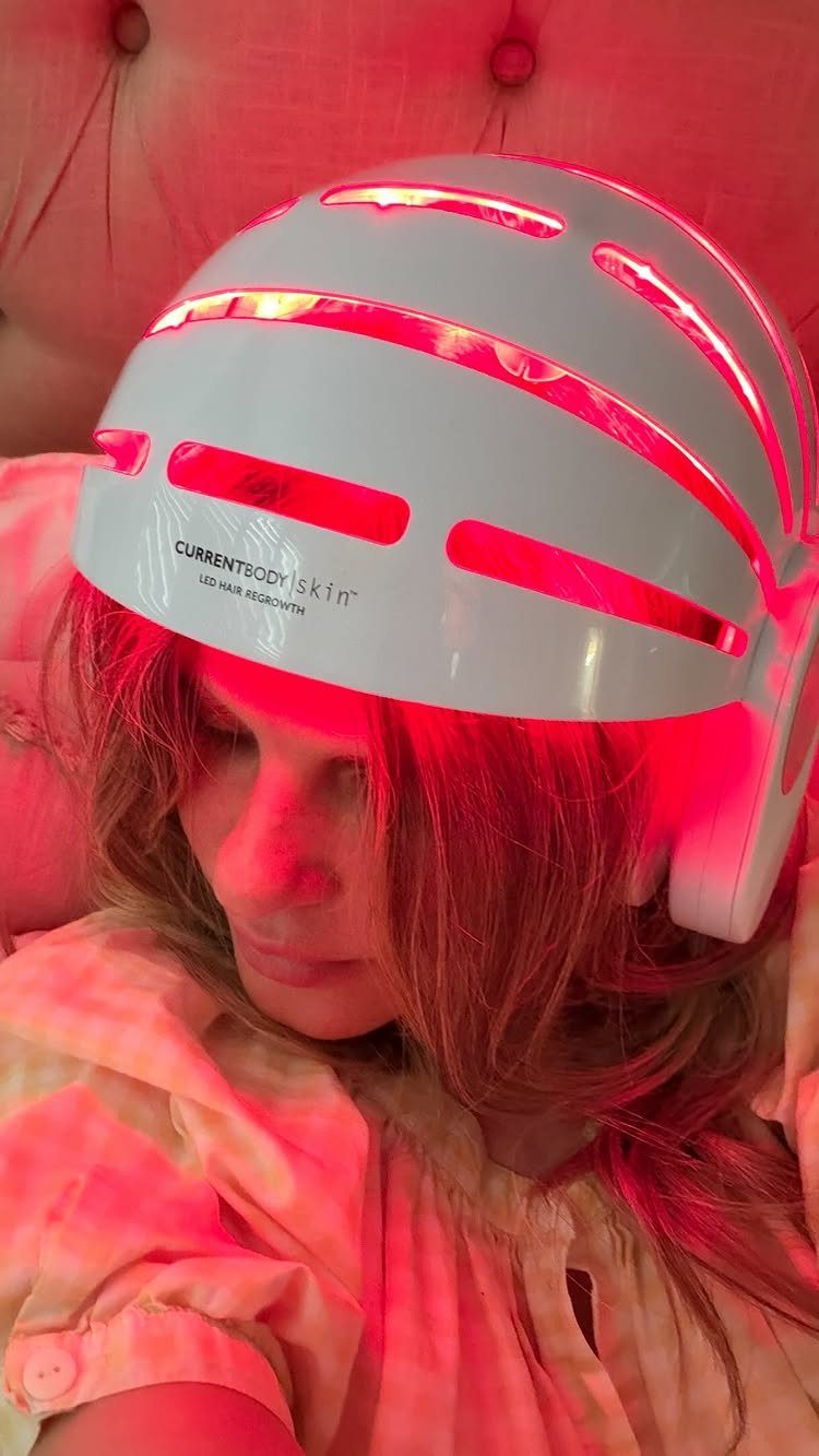 Woman wearing a white red light therapy helmet emitting a red glow over hair.