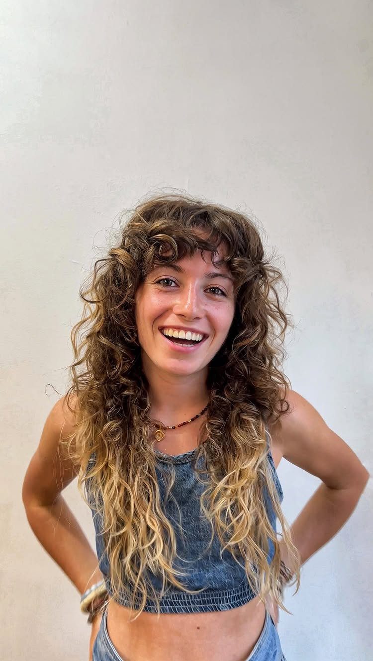Woman with long curly brown hair and bangs wearing a denim crop top.