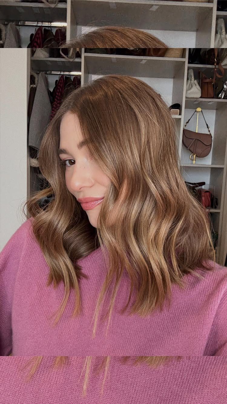 Woman with wavy light brown shoulder-length lob haircut wearing a pink sweater.