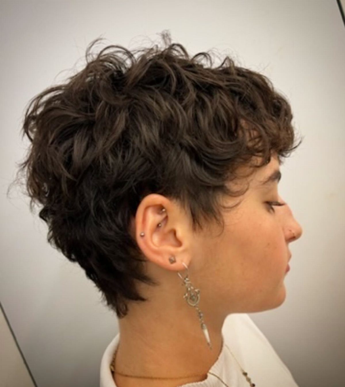 Person with a short, curly pixie cut and voluminous dark hair in profile.