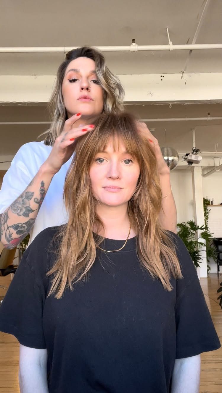 Woman with a layered, textured shag haircut and bangs in a bright studio.
