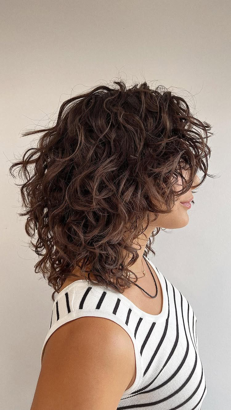 Woman with curly brown shoulder-length shag haircut and messy waves in profile.