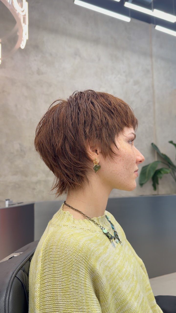 Person with a reddish-brown tousled pixie haircut and choppy layers in profile.