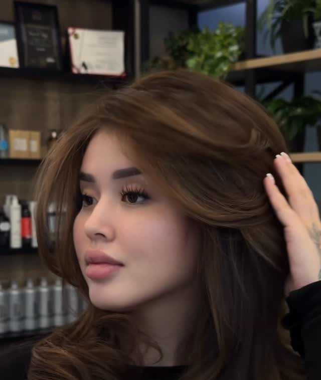 Woman with long wavy brown hair and side-swept bangs in a hair salon.