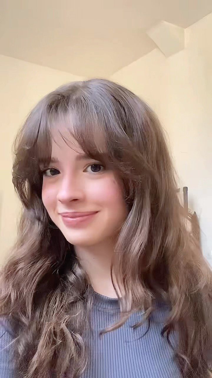 Young woman with long wavy brown hair and center-parted curtain bangs.