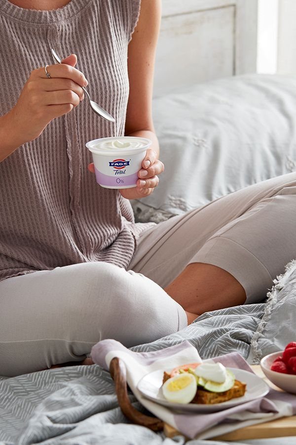 Woman eating Greek yogurt with eggs and raspberries on a bed tray.