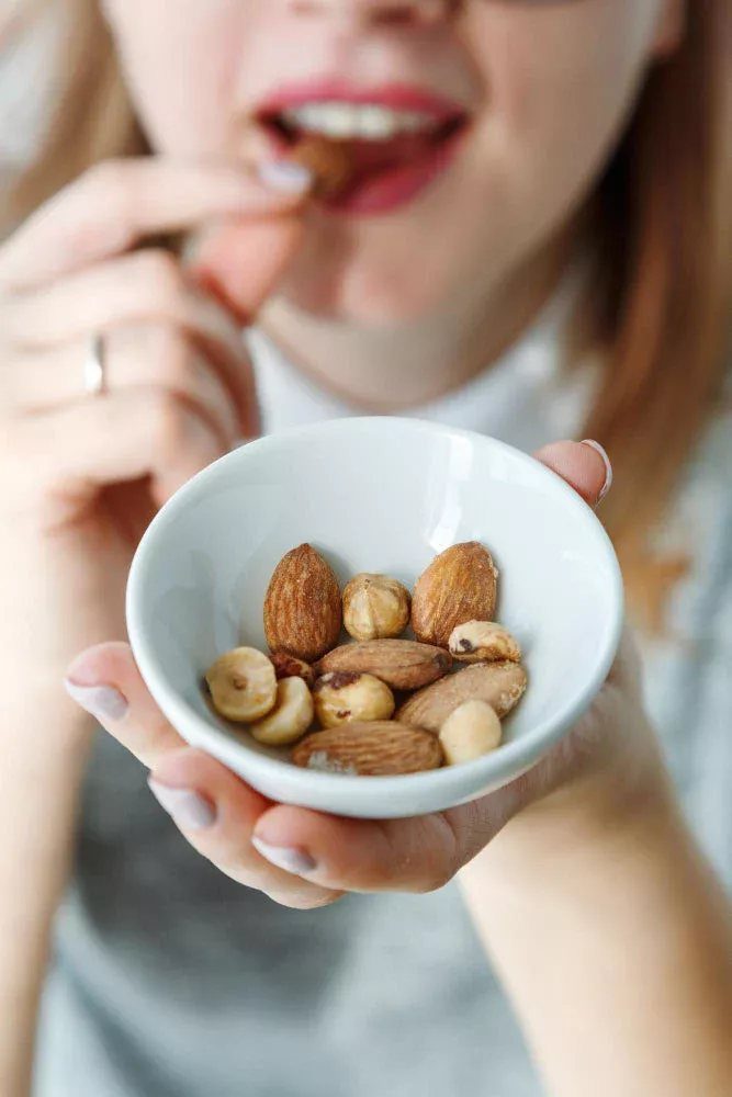 Small white bowl of mixed nuts held by a person eating one.